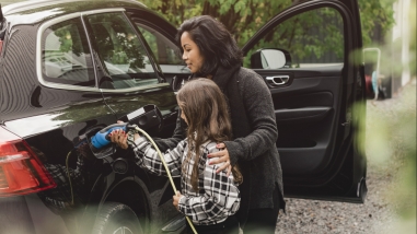Mid adult woman teaching daughter to charge electric car at charging station