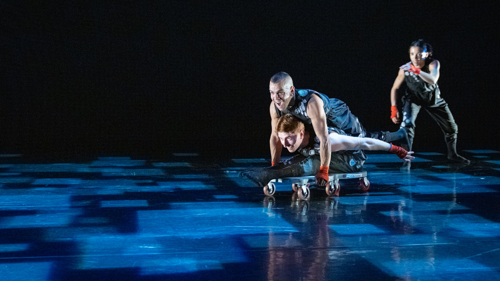 Three dancers on a dark stage with square light projections.