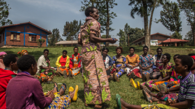 A group of women in Rwanda sitting together in a circle, one woman is standing and speaking.